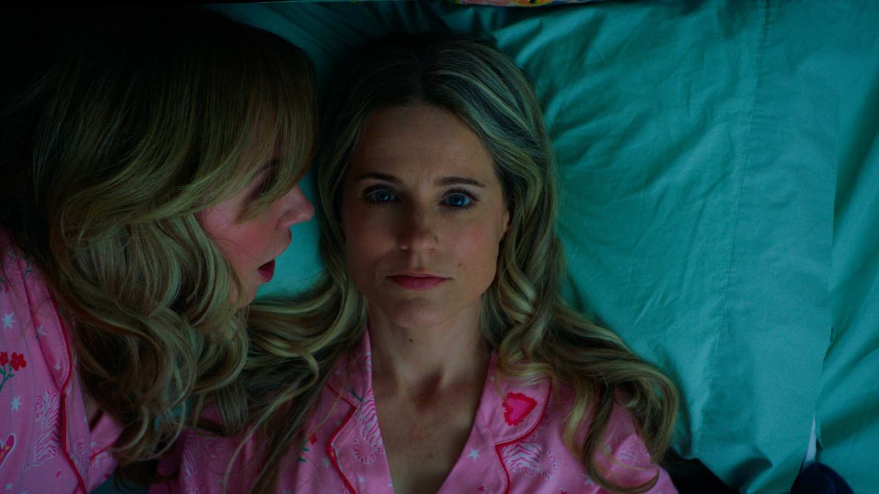 Two women in pink pajamas lie on teal bedding during a tense nighttime conversation.